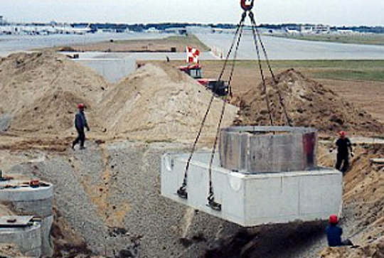 Construction workers install a large rectangular concrete structure into a trench at a development site.