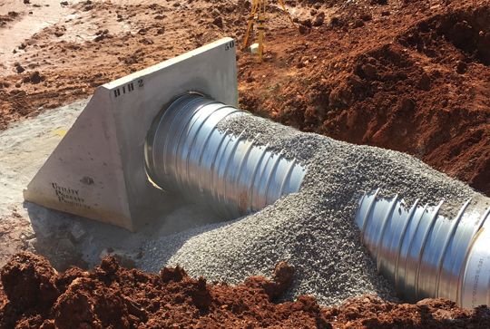 Metal drainage pipe installed in a construction site with surrounding gravel and soil.