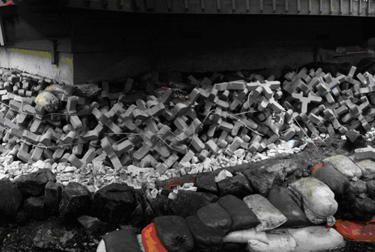 Concrete blocks and stacked sandbags under a bridge, used for stability and flood prevention.