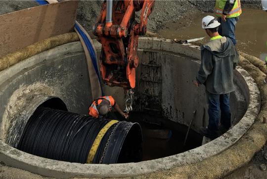 Construction workers installing a large pipeline in a concrete structure using heavy machinery.
