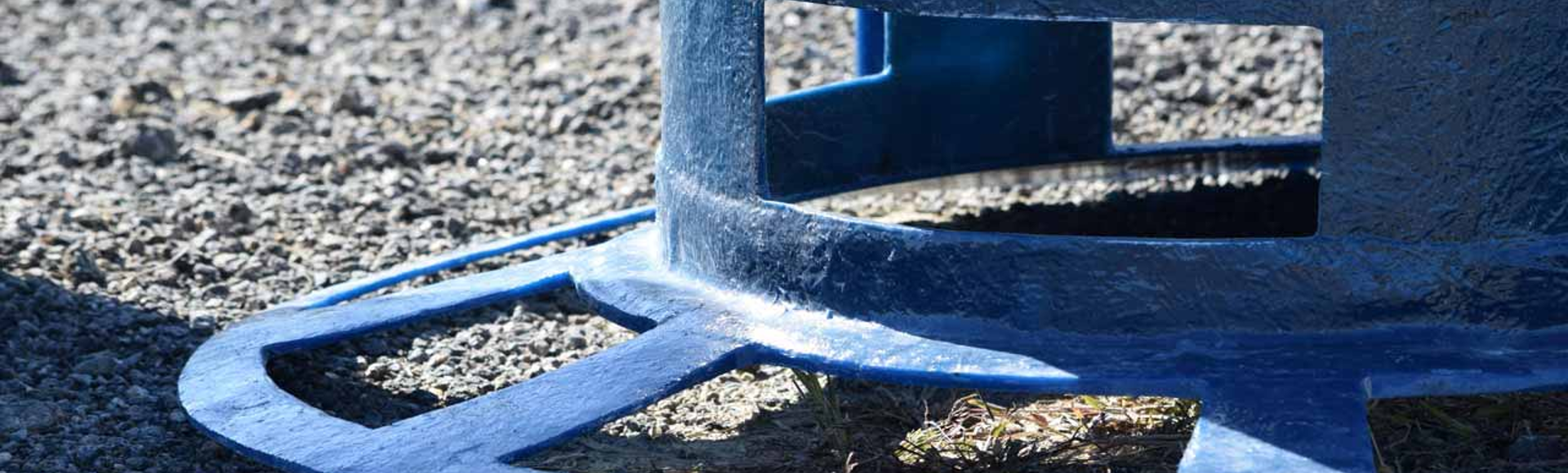 Close-up of a blue metal structure with openings, positioned on a gravel surface, partially covering a patch of grass.