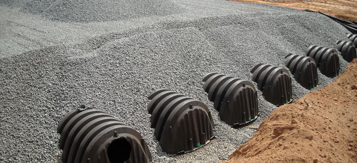 ChamberMaxx plastic stormwater chambers partially buried in gravel at a construction site.