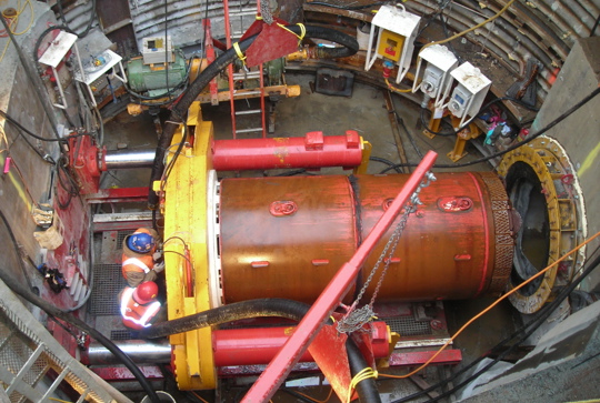 Workers inspecting machinery in an underground tunnel construction site, surrounded by industrial equipment and cables.